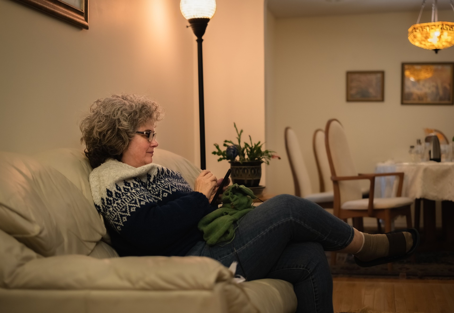 Mature woman wearing winter sweater checking her smart phone while holding her knitting on her lap